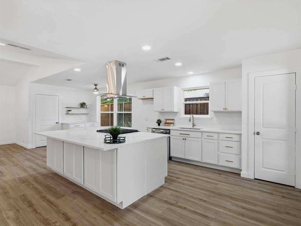 2500 Teakwood Lane, Plano, TX 75075 White kitchen featuring a large island with a cooktop, stone countertops, white shaker-style cabinetry, and wood-finish flooring