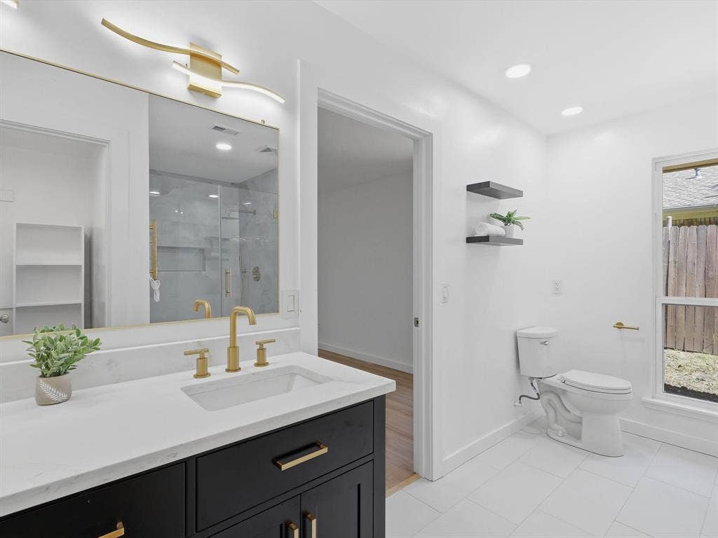 2500 Teakwood Lane, Plano, TX 75075 Modern bathroom featuring a black vanity with a white countertop, gold-finish fixtures, and white tile flooring