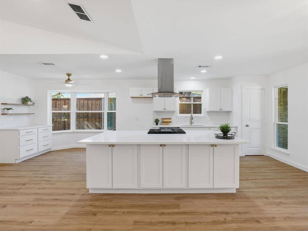 2500 Teakwood Lane, Plano, TX 75075 Open-concept kitchen featuring an island with a cooktop, wood-finish flooring, white cabinetry, and recessed lighting