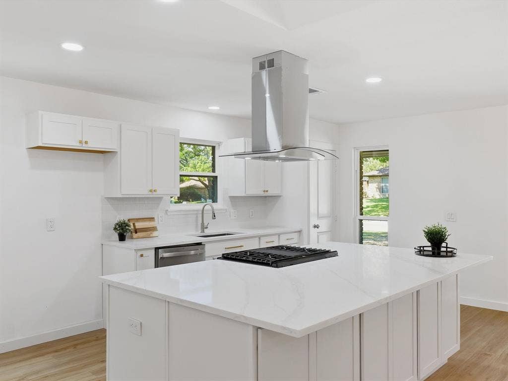 2500 Teakwood Lane, Plano, TX 75075 White shaker cabinetry with gold-finish hardware, stainless steel appliances, white subway tile backsplash, white countertop island with integrated cooktop, and wood-finish flooring