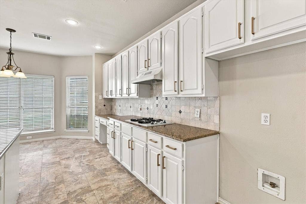 2412 Clearwood Lane, Flower Mound, TX 75028 A BEAUTIFUL BLEND OF FORM AND FUNCTION! An impressive wall of freshly painted white cabinetry with brushed gold, warm granite countertops, decorative tile backsplash, and built-in gas cooktop provide generous storage and preparation space.