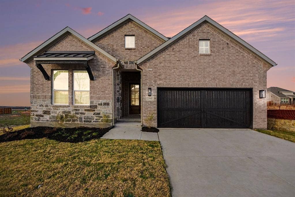 Brick and stone exterior facade featuring a covered front entryway, metal window awning, and a two-car garage with carriage-style doors
