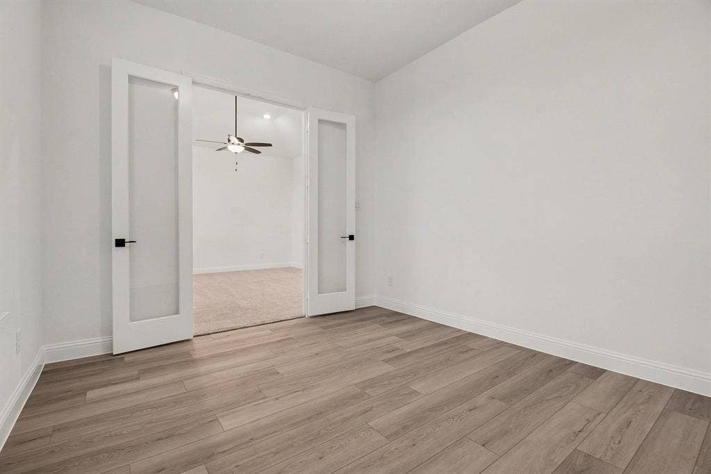 Room featuring wood-finish flooring, white walls, and white French doors with glass panels and matte black hardware