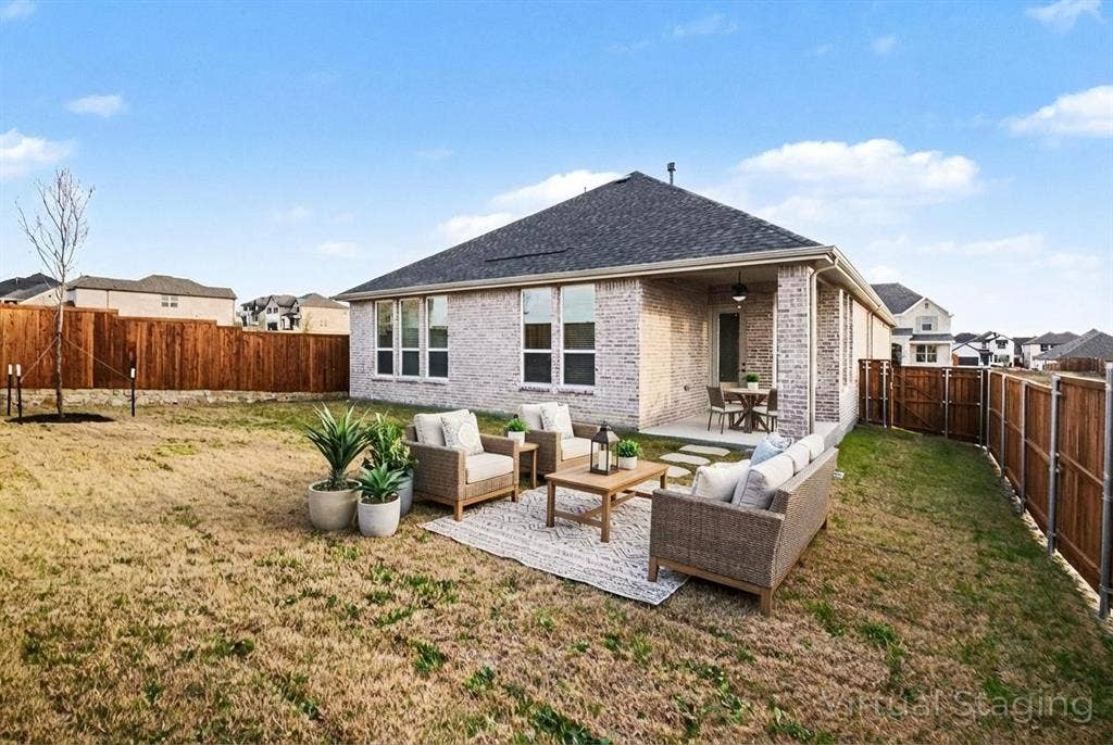 Rear elevation featuring light-toned brick masonry, a covered concrete patio, multi-pane windows, and a fully enclosed wood privacy fence