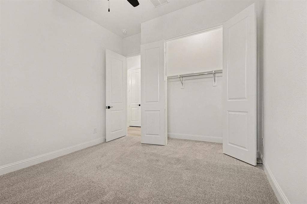 Neutral-toned carpeting, two-panel interior doors with matte black hardware, and a reach-in closet featuring a built-in metal shelving rod