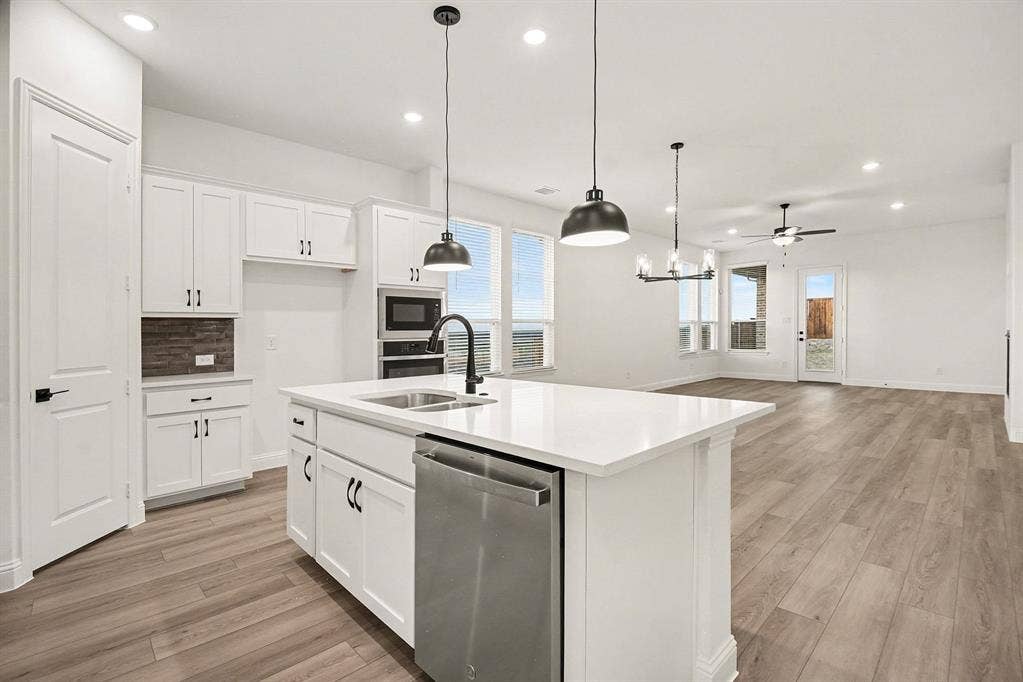 Kitchen featuring a central island with a solid surface countertop, white shaker-style cabinetry, stainless steel built-in appliances, pendant lighting, and wood-finish flooring