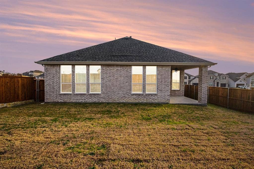 Brick exterior featuring a hip roof, five large windows, a covered patio with a ceiling-mounted fan, and perimeter wood fencing