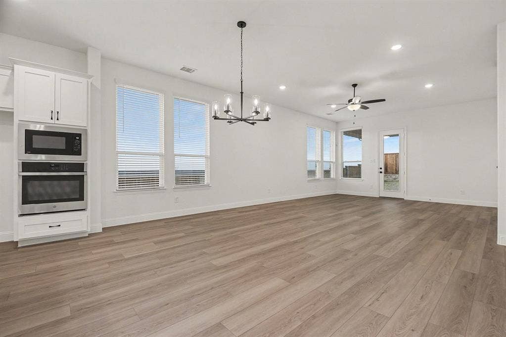 Open concept area featuring wood-finish flooring, built-in stainless steel double wall ovens, a multi-arm chandelier, recessed lighting, and a ceiling fan