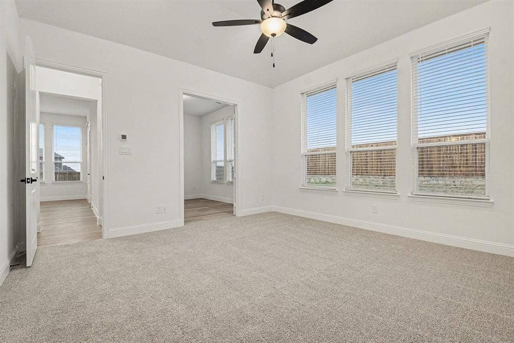 Neutral-toned carpeting, multi-pane windows with horizontal blinds, and a central ceiling fan with integrated lighting