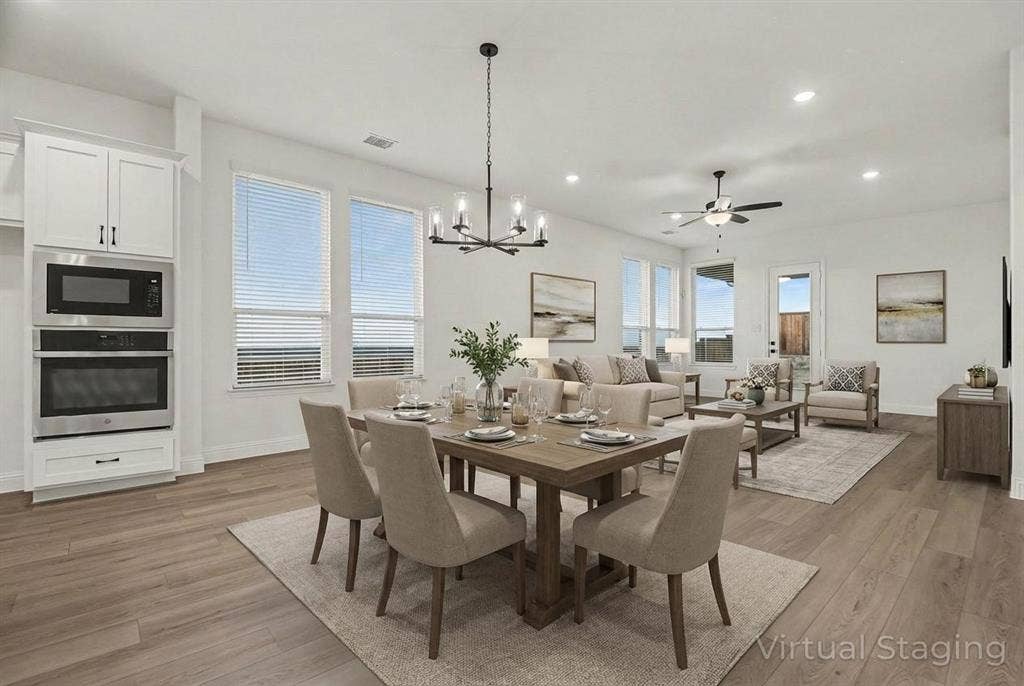 Open-concept interior featuring wood-finish flooring, recessed lighting, built-in stainless steel double wall ovens, a multi-arm chandelier, and multiple windows