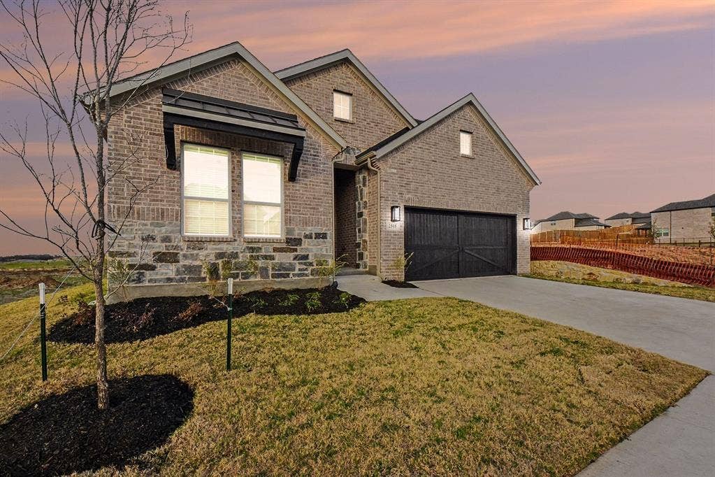 Brick and stone facade featuring a metal awning over the front window, dark-toned carriage-style garage door, and concrete driveway