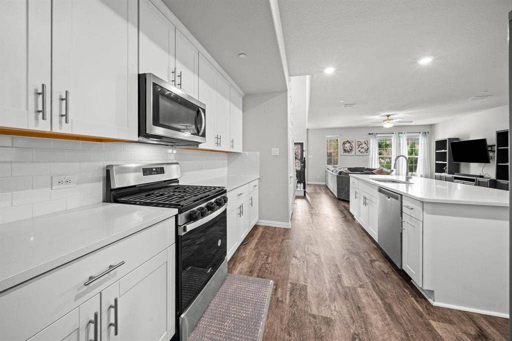 4129 Bullwhip Creek Lane, Sachse, TX 75048 Modern kitchen featuring white cabinetry, stainless steel appliances, light countertops, subway tile backsplash, and wood-finish flooring