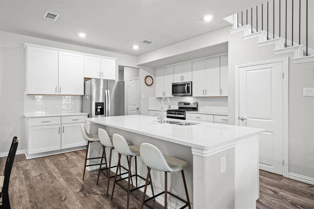 4129 Bullwhip Creek Lane, Sachse, TX 75048 Contemporary kitchen featuring white cabinetry, stainless steel appliances, a center island with countertop seating, and wood-finish flooring