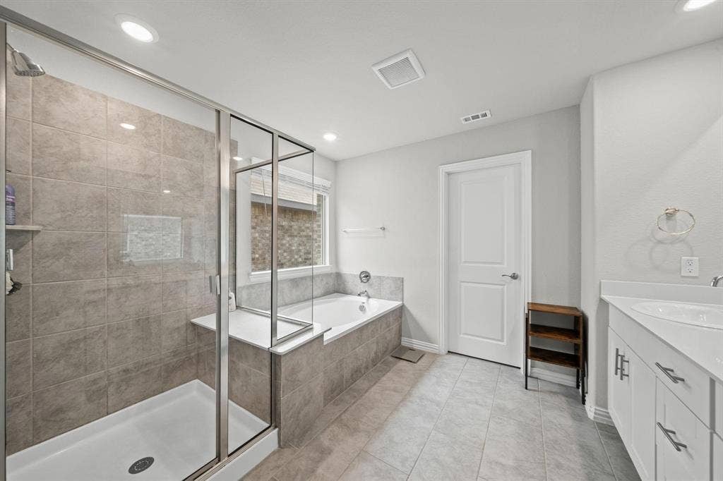 4129 Bullwhip Creek Lane, Sachse, TX 75048 Contemporary bathroom featuring a glass-enclosed shower with tiled walls, a separate built-in bathtub, and a dual-sink vanity with white cabinetry