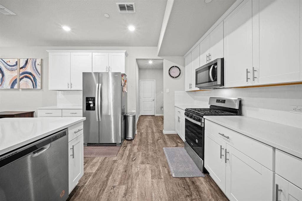 4129 Bullwhip Creek Lane, Sachse, TX 75048 Kitchen featuring white cabinetry, stainless steel appliances, wood-finish flooring, white countertops, and a white subway tile backsplash