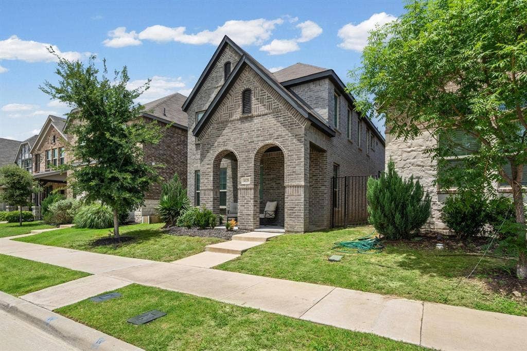 4129 Bullwhip Creek Lane, Sachse, TX 75048 Brick exterior featuring an arched entry, gabled roofline, front porch, and established landscaping
