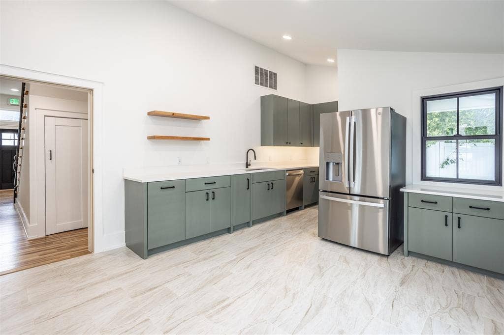 Kitchen featuring sage green cabinetry, white stone-finish countertops, stainless steel appliances, open wood shelving, and tiled flooring