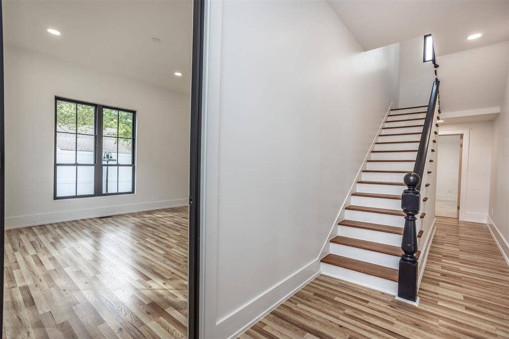Staircase featuring wooden treads, white risers, and a dark-finished newel post, wood-finish flooring throughout, and grid-pane windows with dark frames