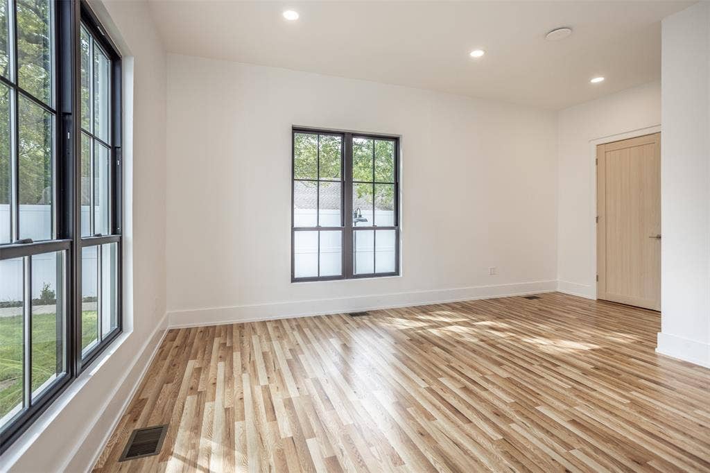 Light-filled room featuring wood-finish flooring, dark-framed multi-pane windows, recessed ceiling lighting, and a light-toned interior door