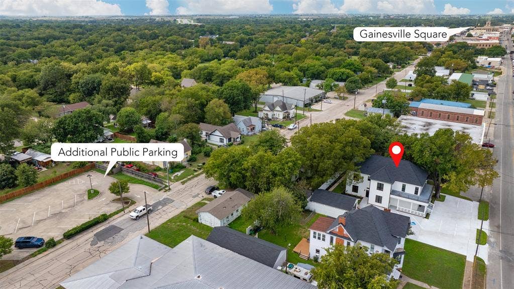 Aerial view showcasing a two-story residence with a dark-toned roof, crisp white exterior, and a concrete driveway