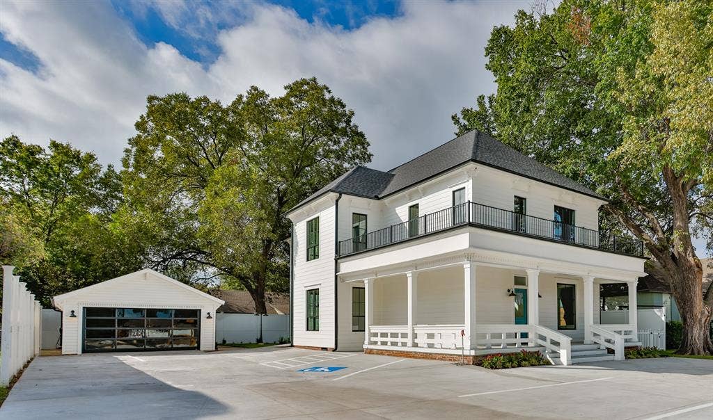 Two-story exterior featuring white horizontal siding, a covered front porch with decorative railings, a second-story balcony with metal railings, and a detached garage with a glass-paneled sectional door