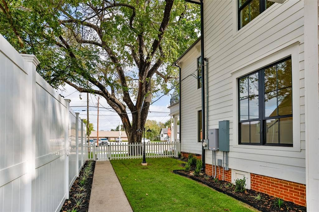 Exterior side yard featuring horizontal lap siding, a brick foundation, full-height white vinyl privacy fencing, a manicured lawn, and a white picket gate