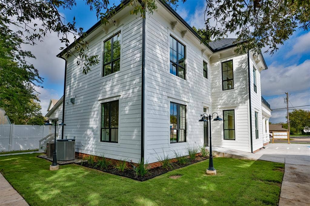 Two-story exterior featuring white horizontal siding, dark-trimmed rectangular windows, a brick foundation, and dual-headed metal post lighting