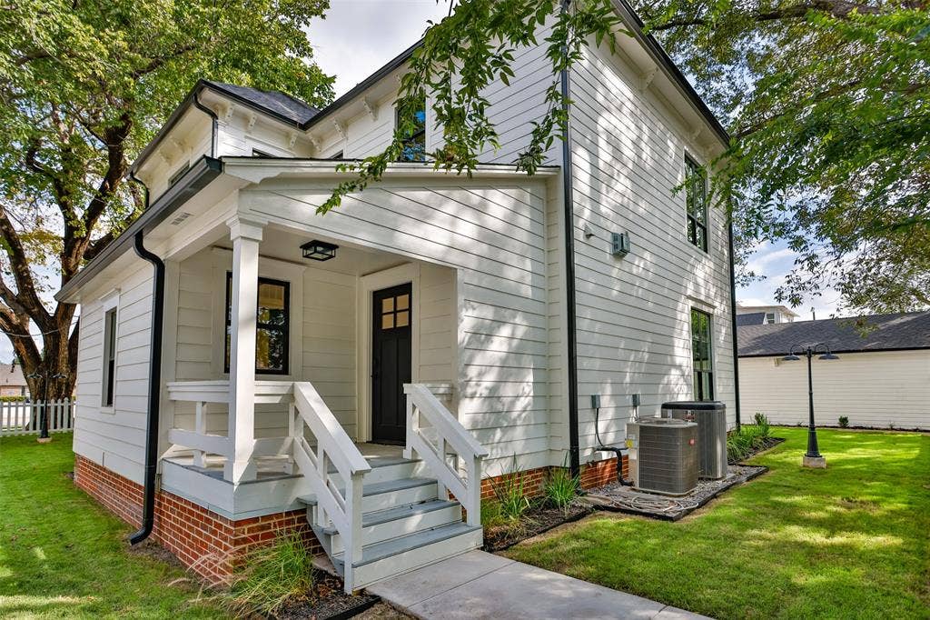 Two-story exterior featuring white horizontal siding, a red brick foundation, a covered porch with a tiered staircase, and dark-framed multi-pane windows