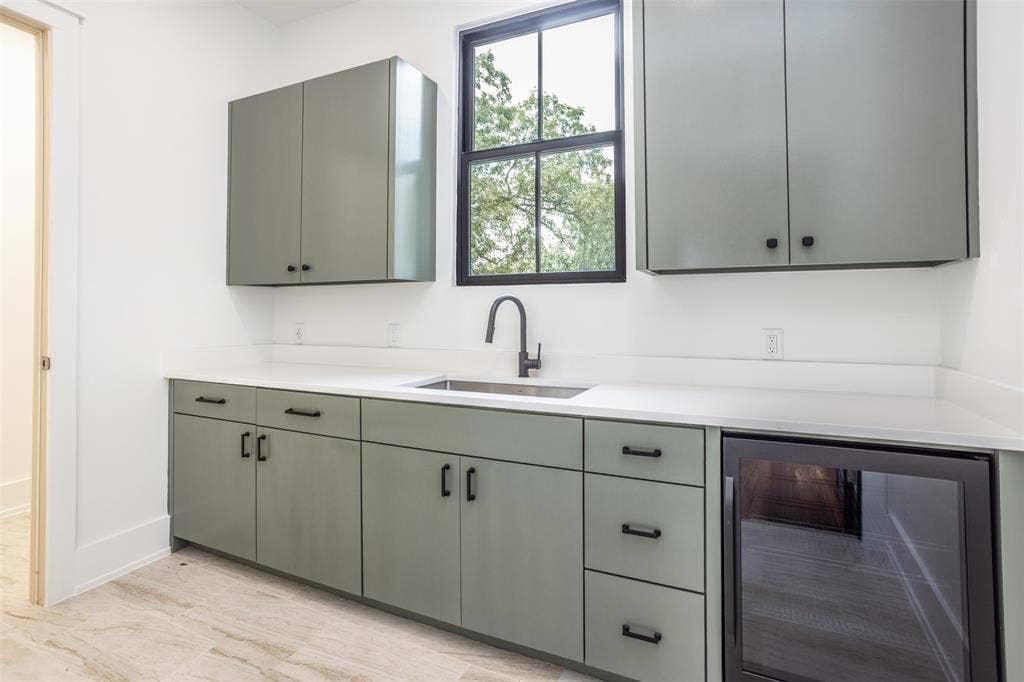 Custom cabinetry featuring a matte finish, solid-surface countertops, an undermount stainless steel sink with a high-arch matte black faucet, and a built-in glass-door beverage refrigerator