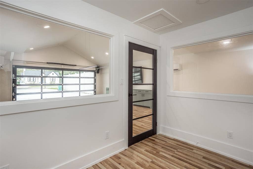 Interior space featuring wood-finish flooring, two large interior windows, and a dark-framed glass paneled door