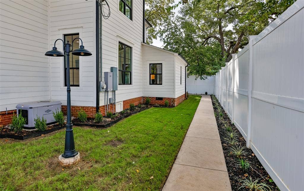 Exterior side yard featuring white horizontal siding, a red brick foundation, concrete walkway, full-height vinyl privacy fencing, and a metal lamppost