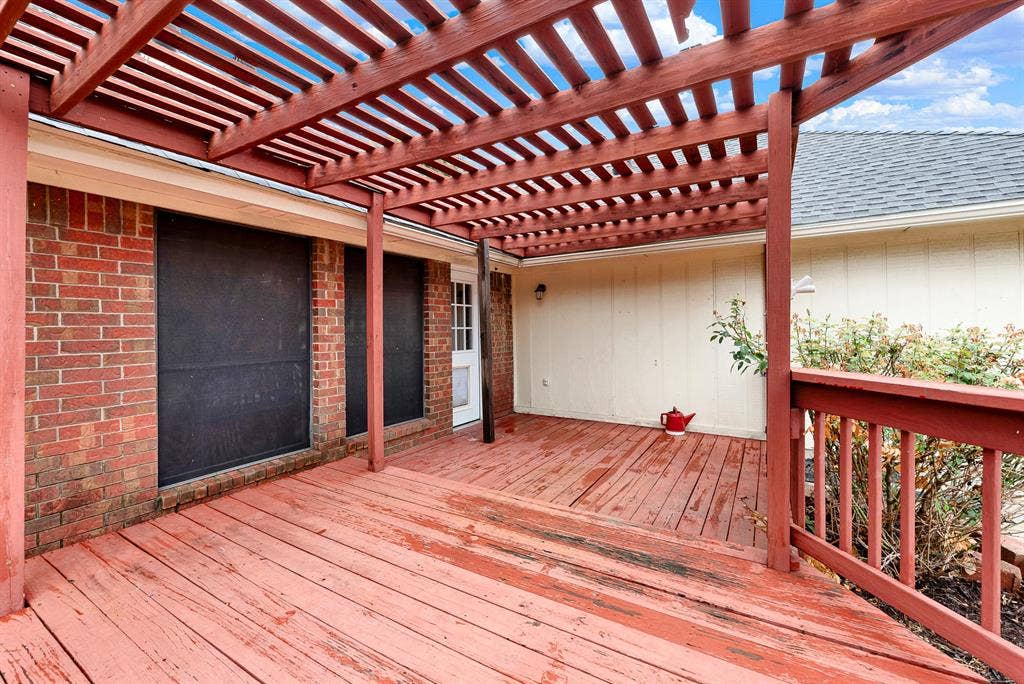 Warm red brick meets extended decking underneath slatted beams, connecting interior doorways directly to outdoor living. Imagine firing up the grill for weekend barbecues while music plays softly under the pergola canopy
