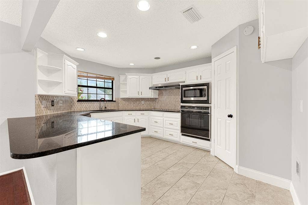 Deep polished granite countertops sweep around bright cabinetry, reflecting crisp recessed ceiling lighting throughout the culinary space. You will love pouring morning juice here while checking emails in this open, functional kitchen