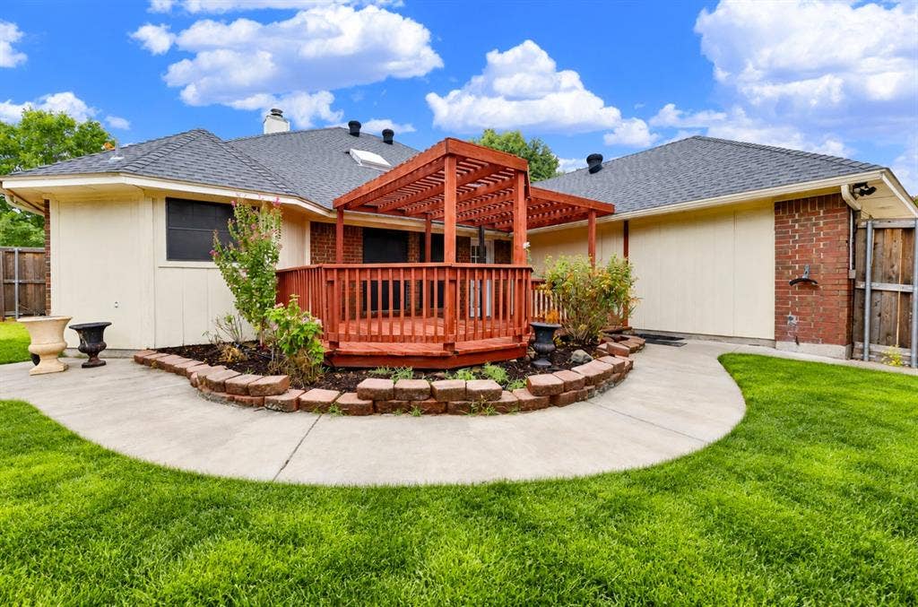 *digitally enhanced*  Curved stone landscaping beds wrap around the raised deck, showcasing structural appeal against the home’s roofline. Unwind here after work, watching evening colors settle over your private backyard oasis.