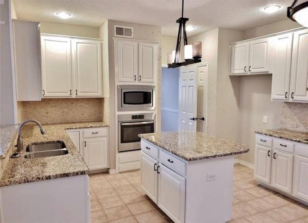 211 Moss Hill Road, Irving, TX 75063 Kitchen featuring white cabinetry, granite countertops, tile backsplash, stainless steel built-in appliances, and a central island