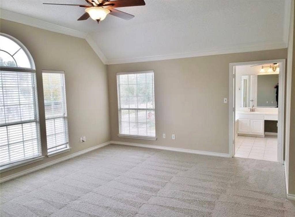 211 Moss Hill Road, Irving, TX 75063 Vaulted ceiling with crown molding, ceiling fan, arched transom window, carpeted flooring, and an adjoining bathroom with a vanity