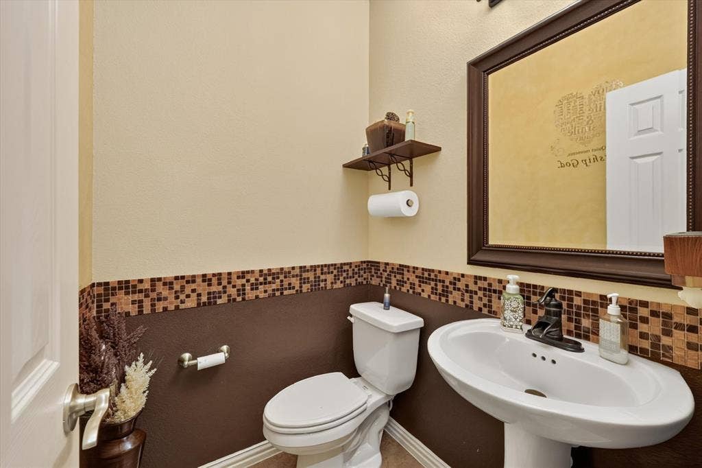 902 Nikki Drive, Cedar Hill, TX 75104 Pedestal sink with dark-toned faucet, wall-mounted mirror, and tile wainscoting