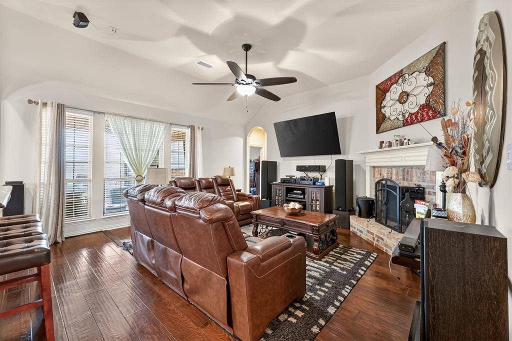 902 Nikki Drive, Cedar Hill, TX 75104 Vaulted ceiling with a ceiling fan, wood-finish flooring, multiple windows, and a brick fireplace with a white mantel