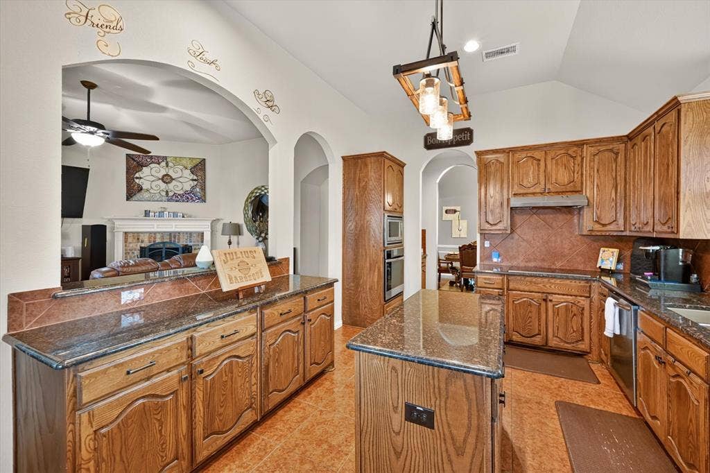902 Nikki Drive, Cedar Hill, TX 75104 Kitchen featuring wood-finish cabinetry, granite countertops, tile flooring, an integrated double oven, and a central island