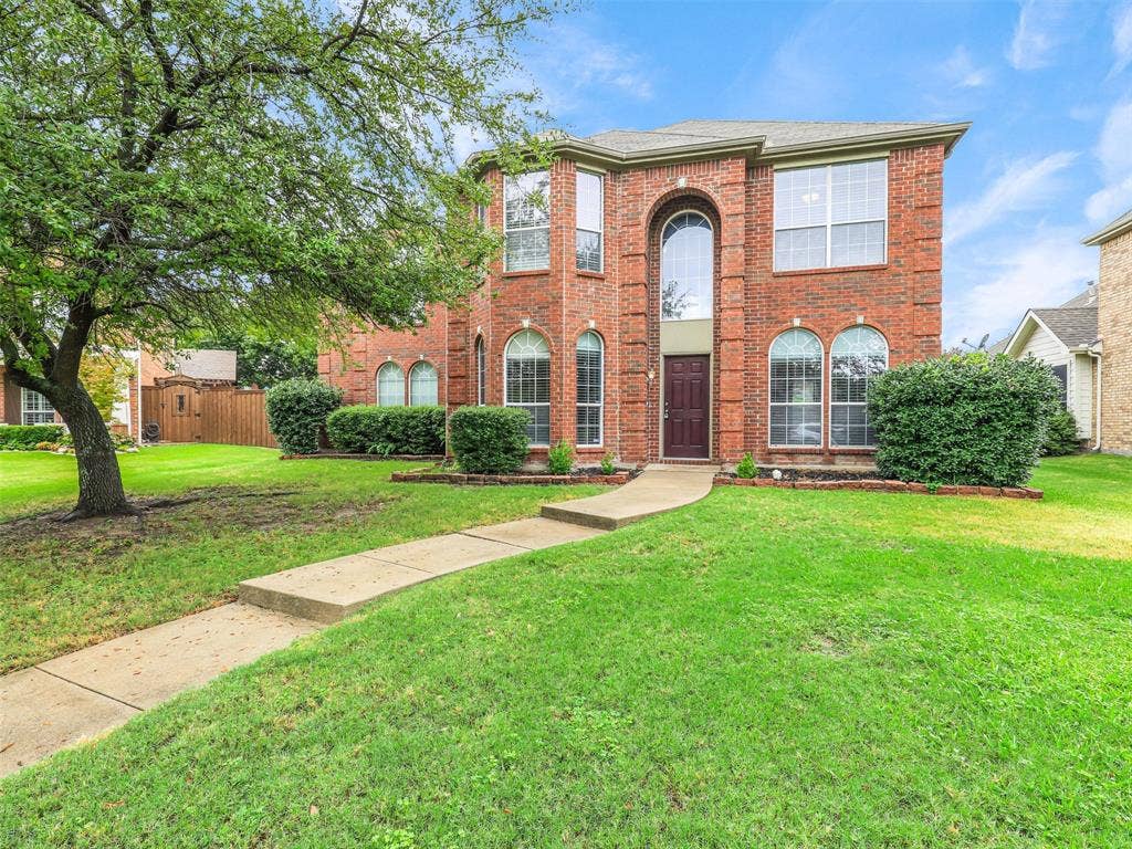 7419 Ravenhill Drive, Frisco, TX 75035 Brick facade with multiple arched windows, two-story architectural design, mature front yard tree, and front entry walkway