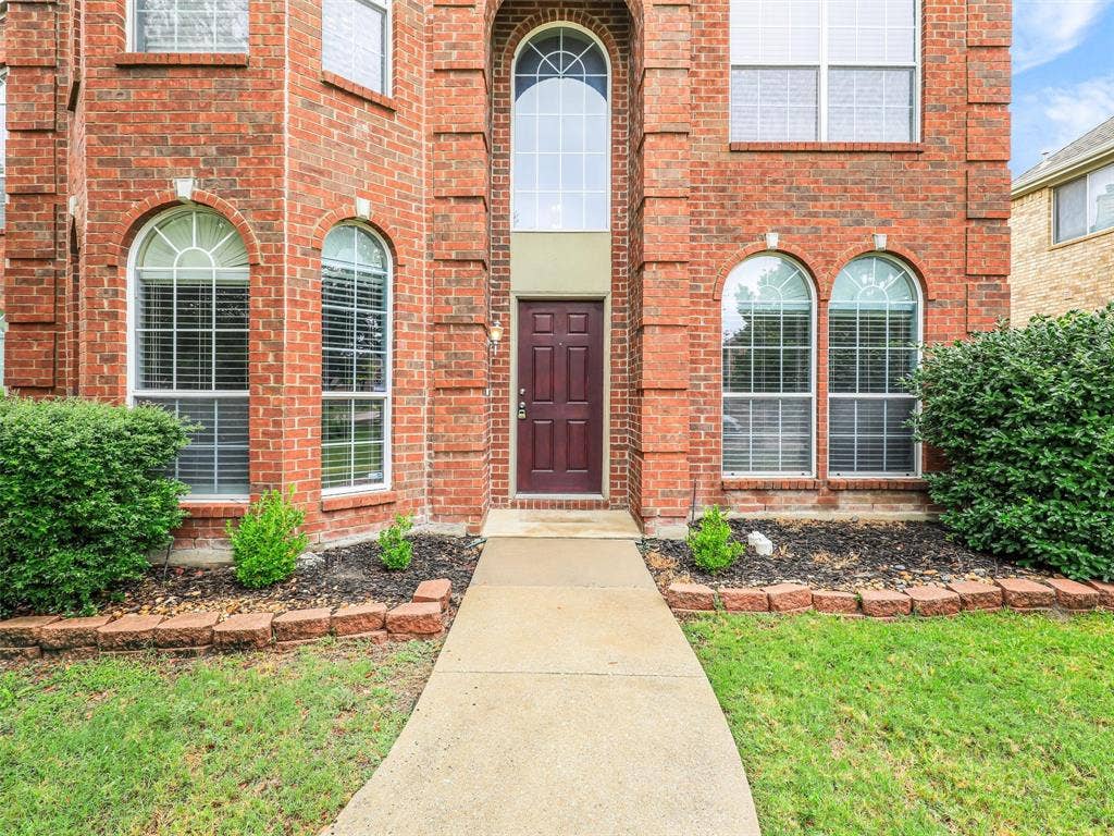 7419 Ravenhill Drive, Frisco, TX 75035 Brick facade with arched window details, a prominent two-story entry window, and an inviting walkway leading to the front door