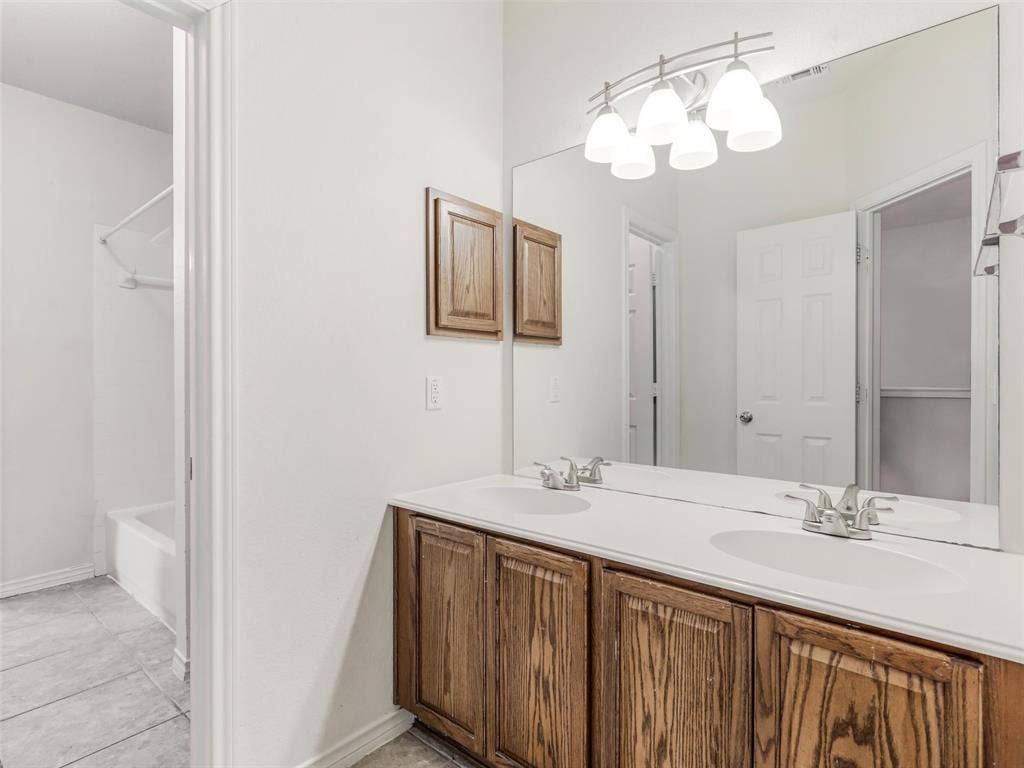 7419 Ravenhill Drive, Frisco, TX 75035 Dual vanity with white countertops, wood-finish cabinetry, and a full-width mirror