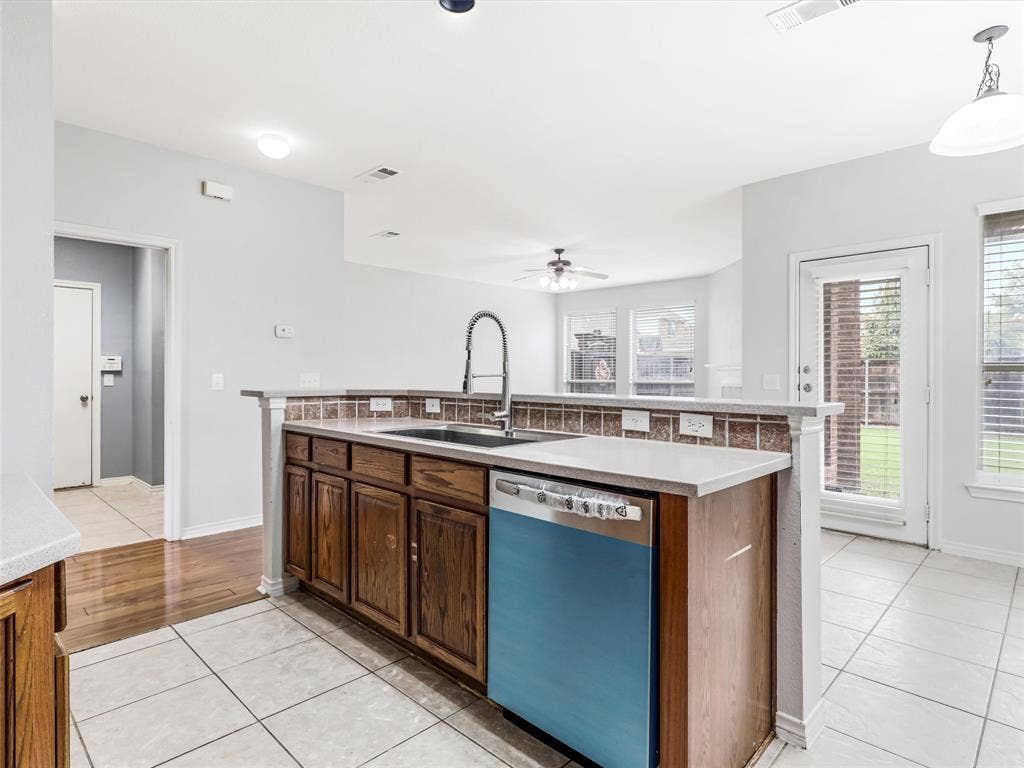 7419 Ravenhill Drive, Frisco, TX 75035 Kitchen island featuring wood-finish cabinetry, a single basin sink with a gooseneck faucet, light-toned countertops, and a tiled backsplash