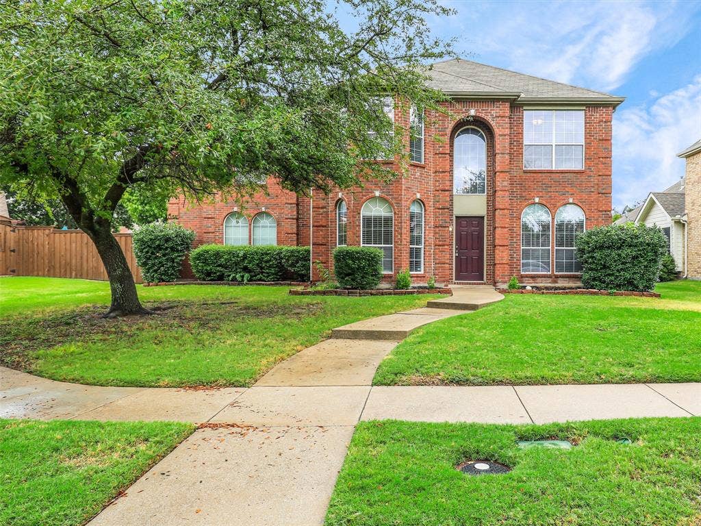 7419 Ravenhill Drive, Frisco, TX 75035 Red brick exterior with arched windows, a dark paneled front door, and a curved concrete walkway
