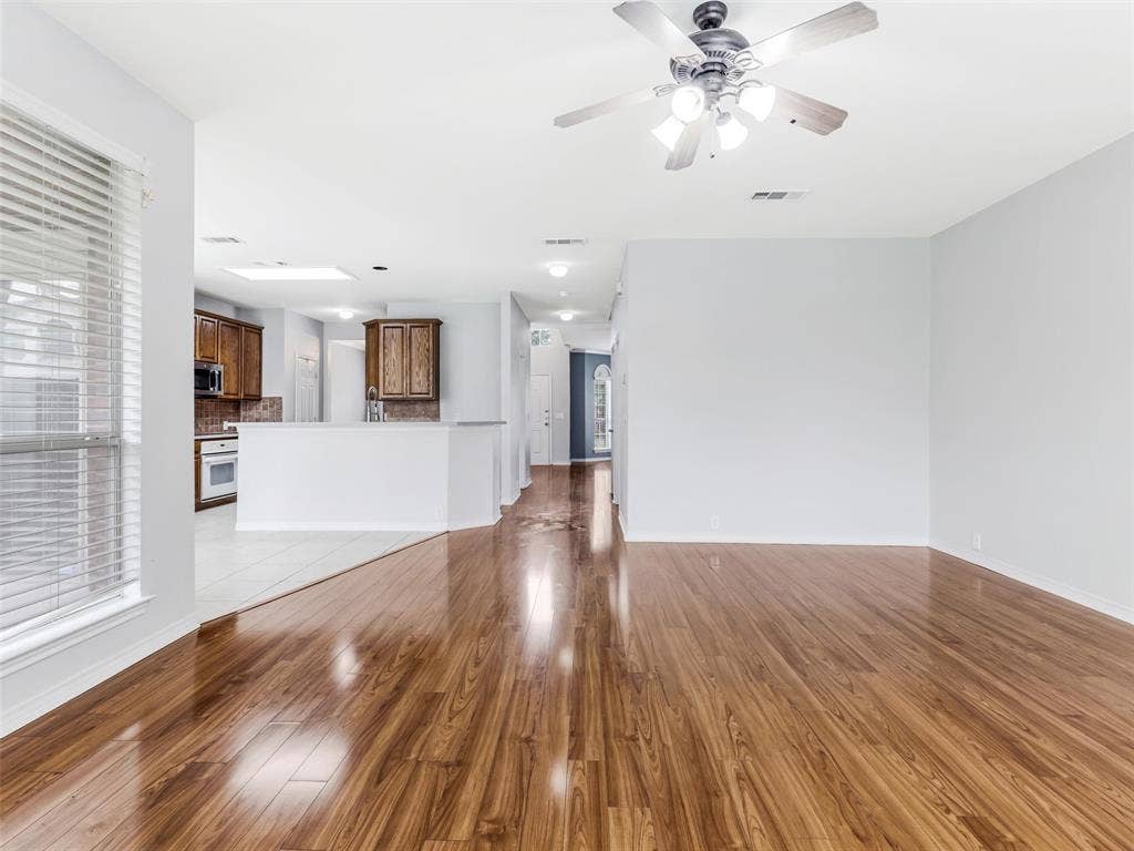 7419 Ravenhill Drive, Frisco, TX 75035 Wood-finish flooring, white wall paint, ceiling fan with integrated lighting, window with horizontal blinds, and a kitchen with wood cabinetry
