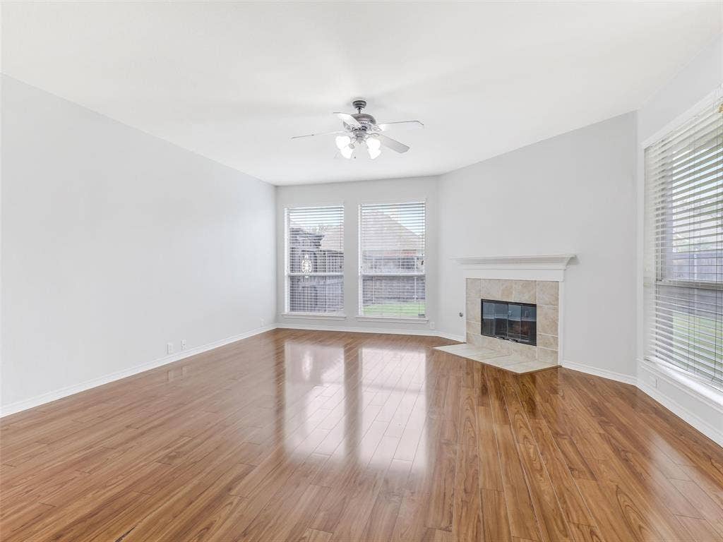 7419 Ravenhill Drive, Frisco, TX 75035 Wood-finish flooring, corner fireplace with tile surround, multiple windows, ceiling fan, and vaulted ceiling