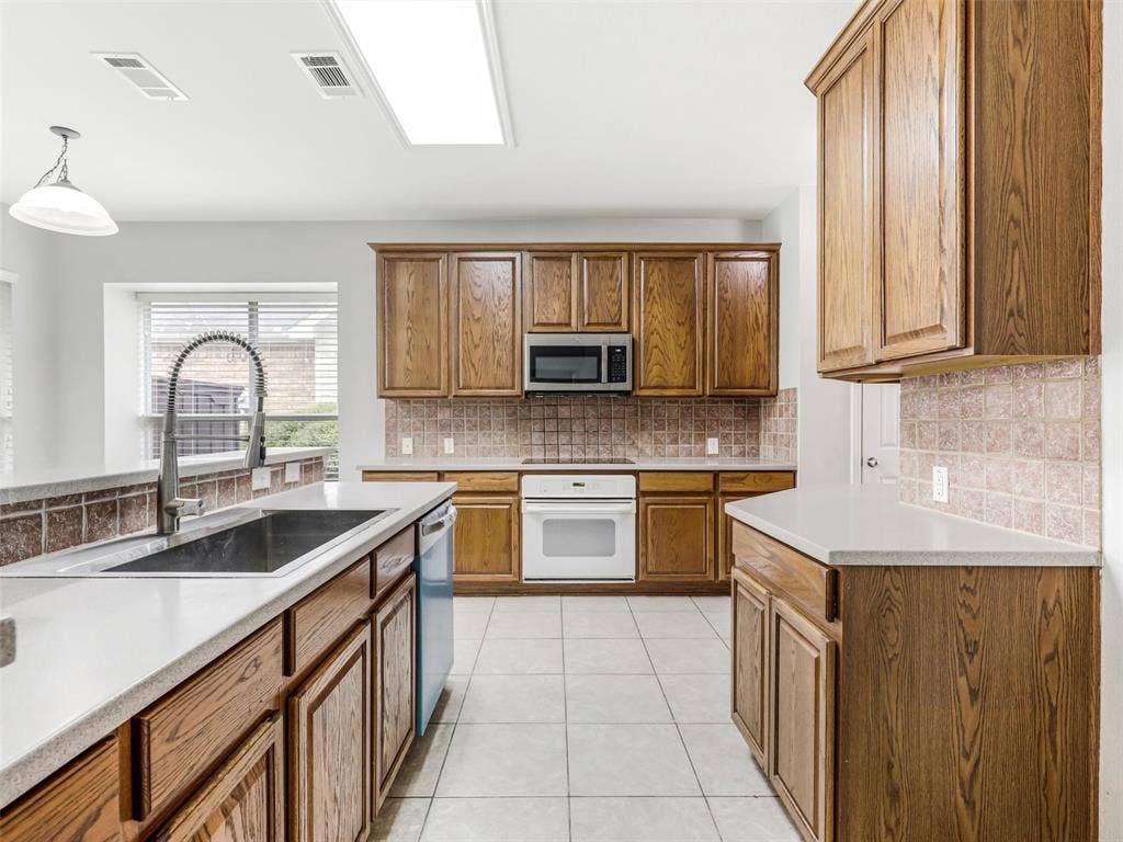 7419 Ravenhill Drive, Frisco, TX 75035 Kitchen featuring wood cabinetry, light countertops, integrated stainless steel microwave, white built-in oven, and tile flooring