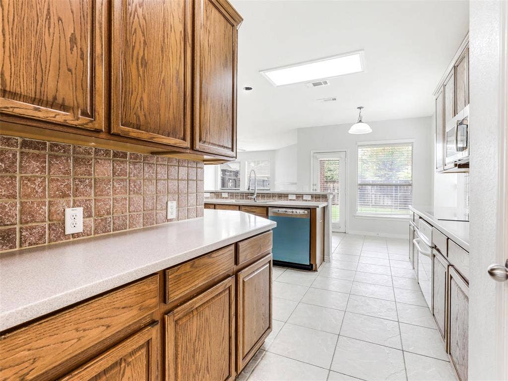 7419 Ravenhill Drive, Frisco, TX 75035 Kitchen featuring wood cabinetry, light-toned countertops, tiled backsplash, and white tile flooring