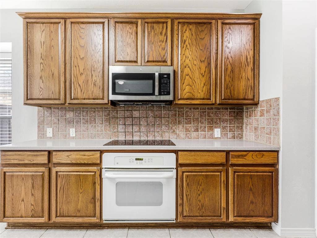 7419 Ravenhill Drive, Frisco, TX 75035 Wood-finish cabinetry paired with a tile backsplash, light-toned countertop, and integrated cooktop