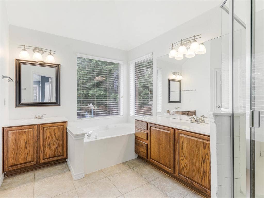 7419 Ravenhill Drive, Frisco, TX 75035 Bathroom featuring a built-in tub, tiled flooring, wood-finish cabinetry, and a large window